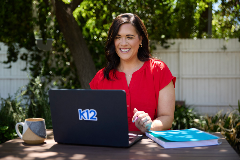 Woman in red shirt using a laptop with K12 logo outdoors