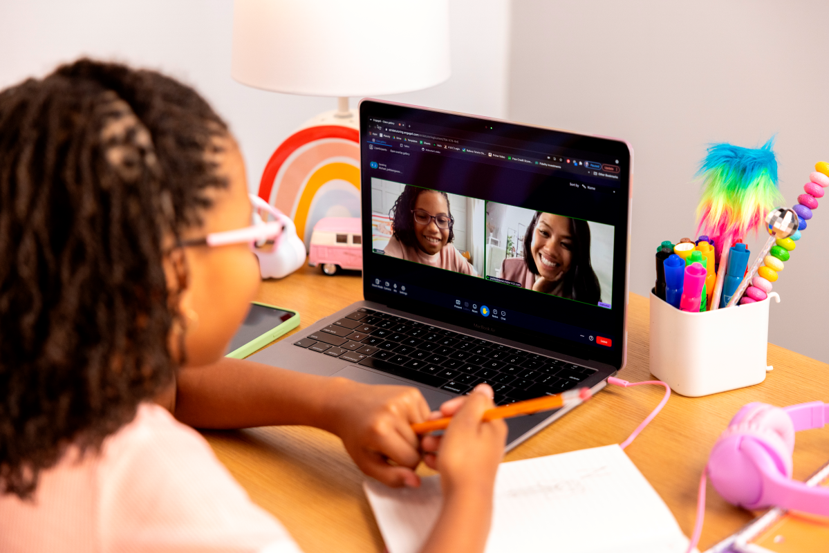 Child using a laptop for a video call with two other people at a desk with colorful stationery.